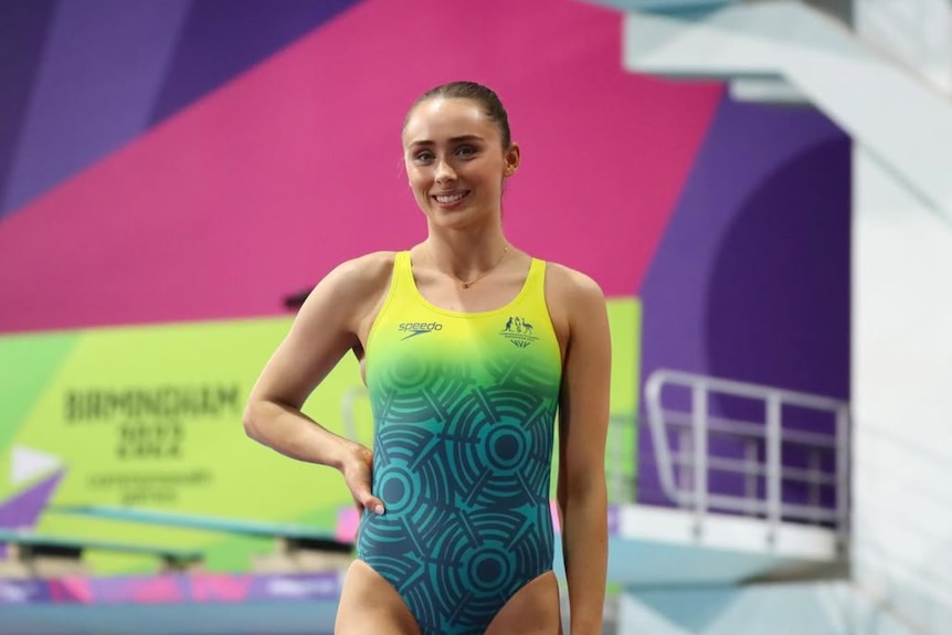 Diver Georgia Sheehan wears an Australian team swimming costume and poses with a smile, with diving board in background