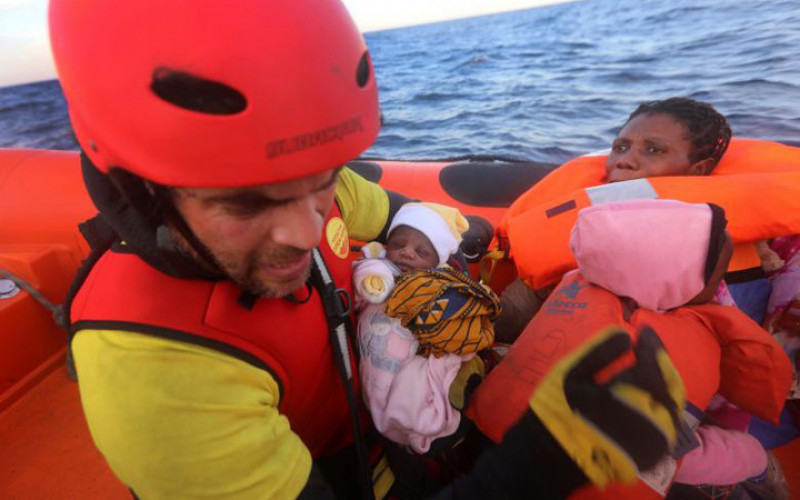 Nhân viên cứu hộ người Tây Ban Nha Asier Renedo trao lại em bé sơ sinh cho một người phụ nữ sau khi cả 2 được cứu khỏi chiếc thuyền cao su.