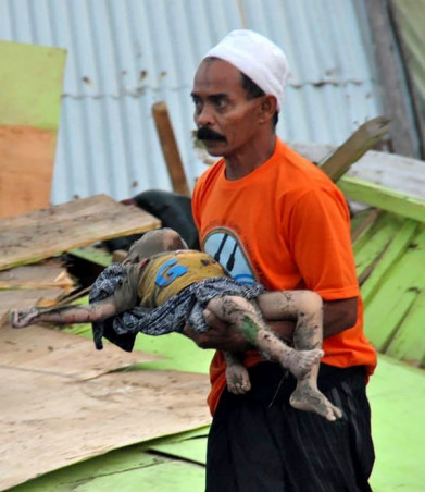 Người đàn ông Palu bế thi thể một đứa trẻ thiệt mạng đầy bùn đất sau sóng thần.