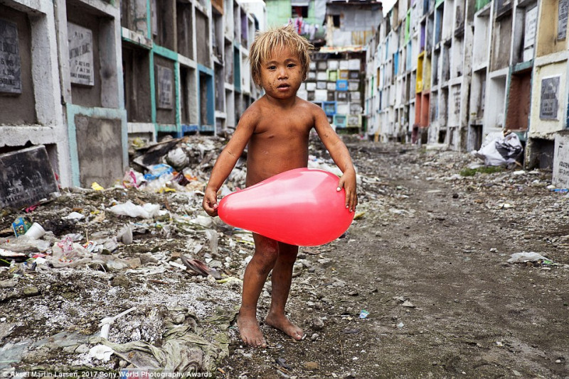 Bức ảnh này được chụp tại một nghĩa trang ở thủ đô Manila, Philippines. Đây là nơi trú ẩn của cộng đồng người vô gia cư, bao gồm rất đông trẻ em. Cậu bé trong ảnh đang chơi đùa cùng một quả bóng mà em may mắn nhặt được. 