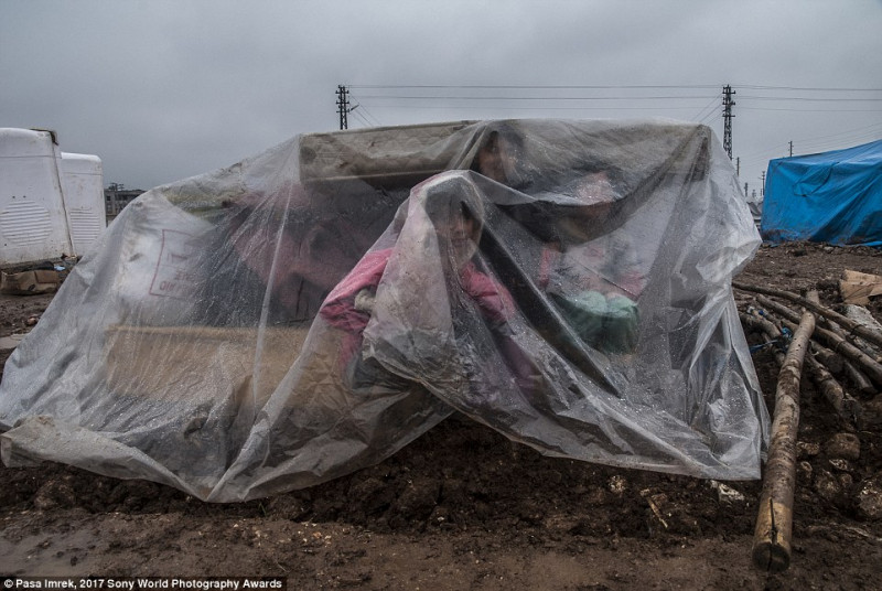 Một em bé tị nạn người Syria trú mưa dưới lớp nilon trong chuyến hành trình tới trại tị nạn ở Thổ Nhĩ Kỳ.
