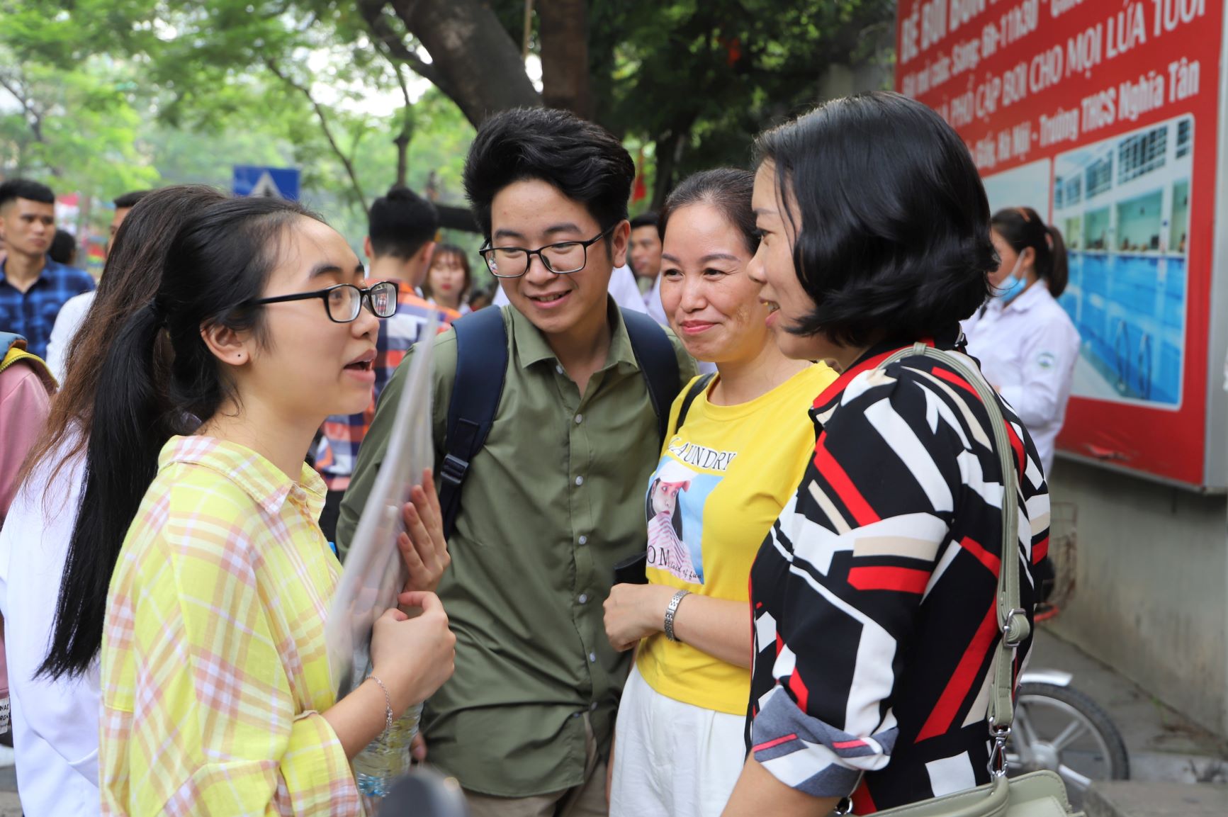 Nhóm phụ huynh, học sinh đứng túm tụm ngay trước cổng trường để trao đổi về kết quả thi. Ai cũng nở nụ cười