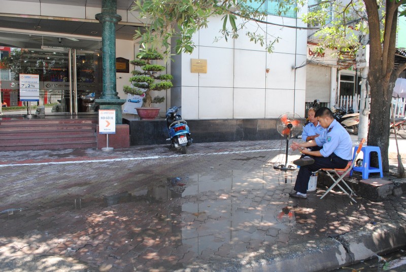 Nhân viên một ngân hàng trên tuyến phố Đại Cồ Việt nghĩ cách phun nước ra nền gạch để giảm nhiệt. 