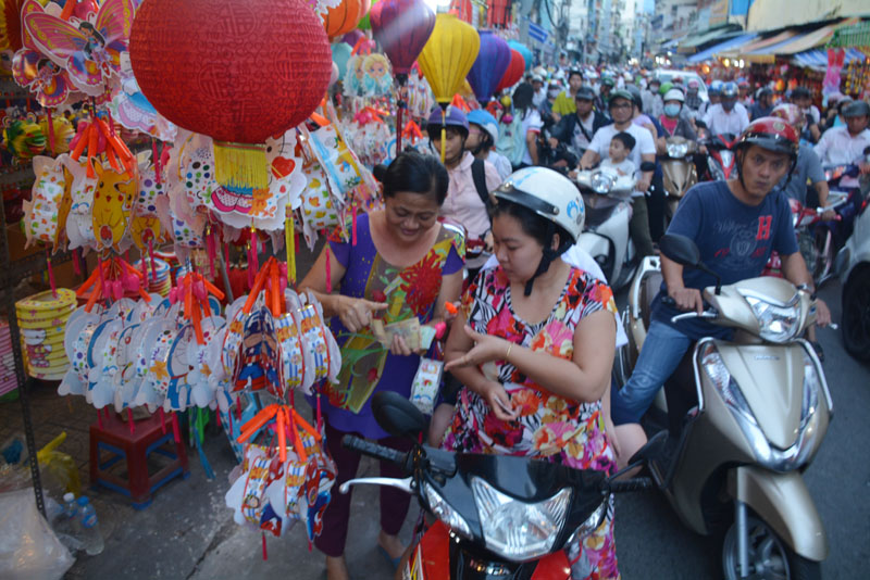 Một người phụ nữ dừng mua lồng đèn giữa dòng xe cộ đông đúc.