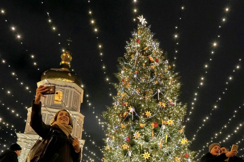 Ở Ukraina, người dân chụp ảnh bên một cây thông Noel được chiếu sáng trước Nhà thờ St Sophia ở trung tâm Kiev hôm 21/12.