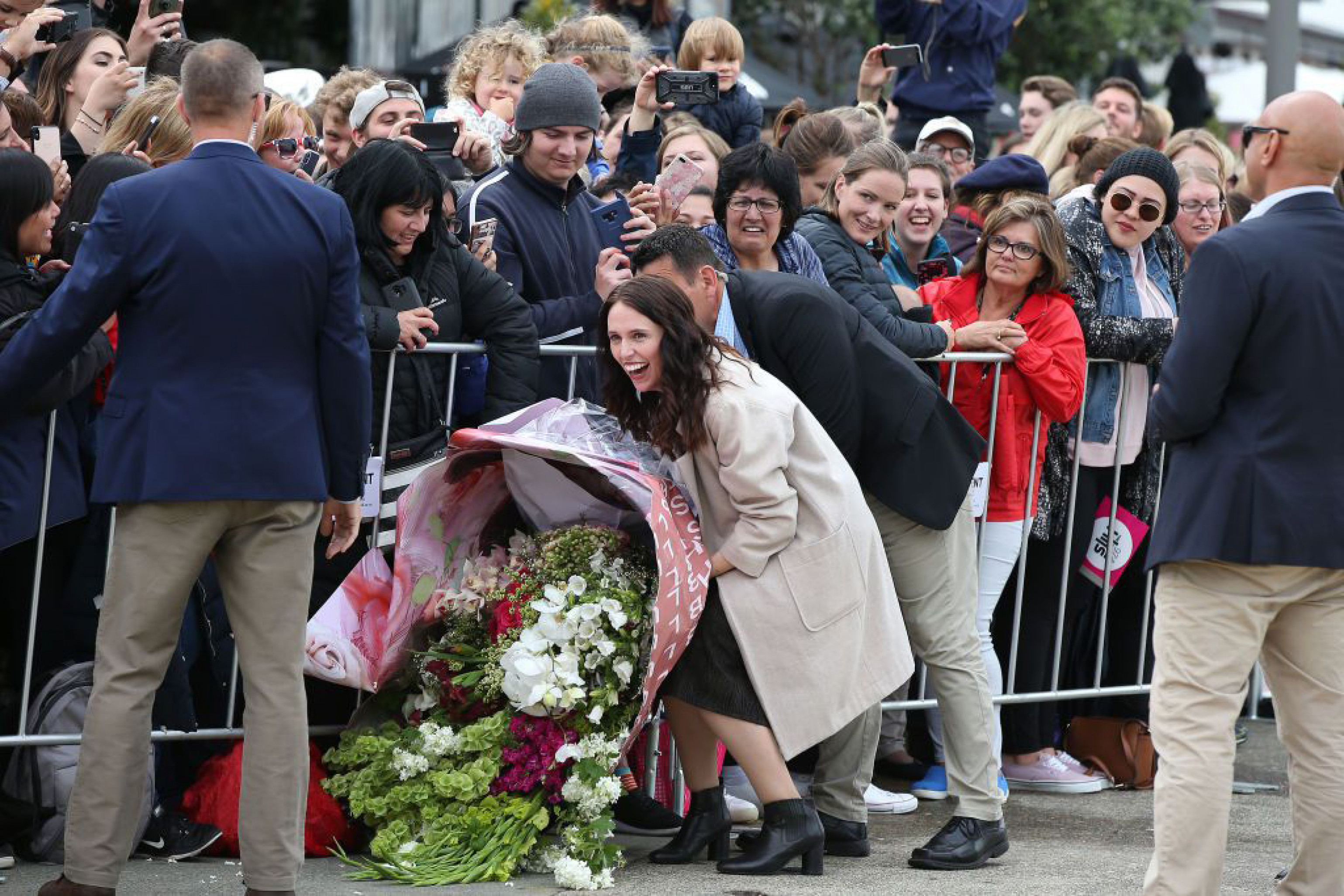 Thủ tướng New Zealand Jacinda Ardern cười tươi nhưng cảm thấy khó khăn khi di chuyển bó hoa khổng lồ giúp Công nương Meghan. 