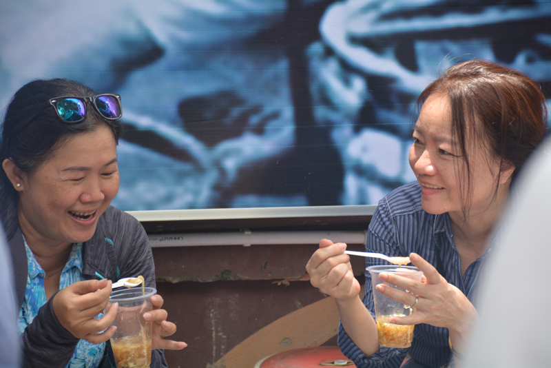 Hai thực khách thích thú thưởng thức đồ ăn tại phố hàng rong Nguyễn Văn Chiêm.