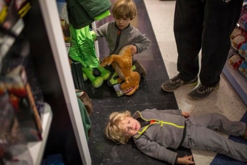 Một cậu bé nằm xuống sàn trong lúc đi mua sắm cùng bố và anh trai. Ảnh: New York Times. 