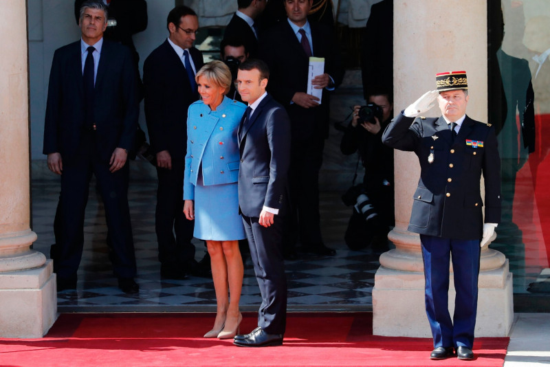 Ông Macron mặc bộ vest tối màu của thương hiệu Pháp Jonas & Cie trị giá 450 euro. Còn phu nhân Brigitte Trogneux mặc đồ màu xanh da trời nhạt, do nhà thiết kế người Pháp Nicolas Ghesquiere thiết kế cho hãng Louis Vuitton.