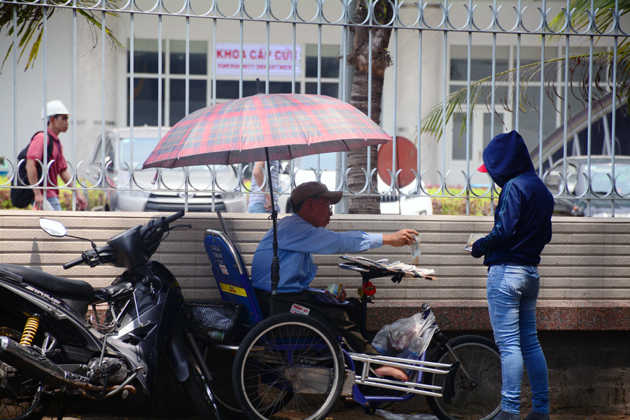 Người đàn ông bán vé số dùng dù để che bớt cái nắng. Trong khi đó, người mua cũng dùng áo trùm kín đầu.