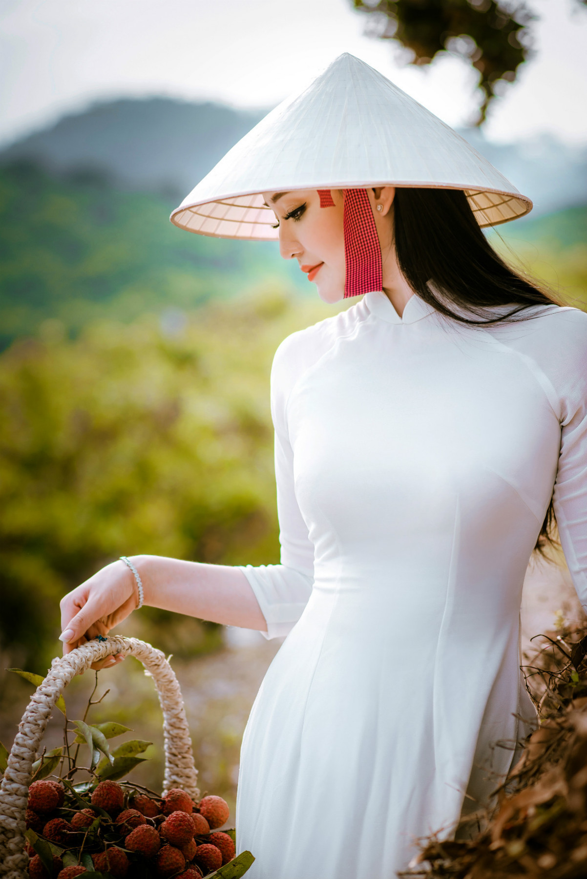 Bộ ảnh này được Julia Wedding thực hiện tại đồi vải Lục Ngạn (Bắc Giang). Trong tà áo dài trắng muốt, người đẹp nổi bật giữa màu xanh của lá, màu đỏ của quả chín, tạo thành một bức tranh mùa hạ rực rỡ mà nên thơ.
