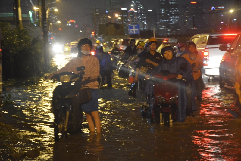 Một người phụ nữ mệt mỏi khi dắt xe qua một đoạt đường dài. Trời mưa cộng với nước dâng cao khiến cho mọi người đuối sức.