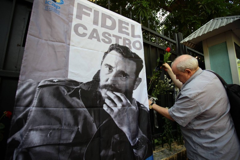 Một người đàn ông đang cài hoa lên bức tường rào trước cổng Đại sứ quán Cuba tại Việt Nam trong ngày diễn ra lễ viếng lãnh tụ Fidel Castro. Ảnh: V.L