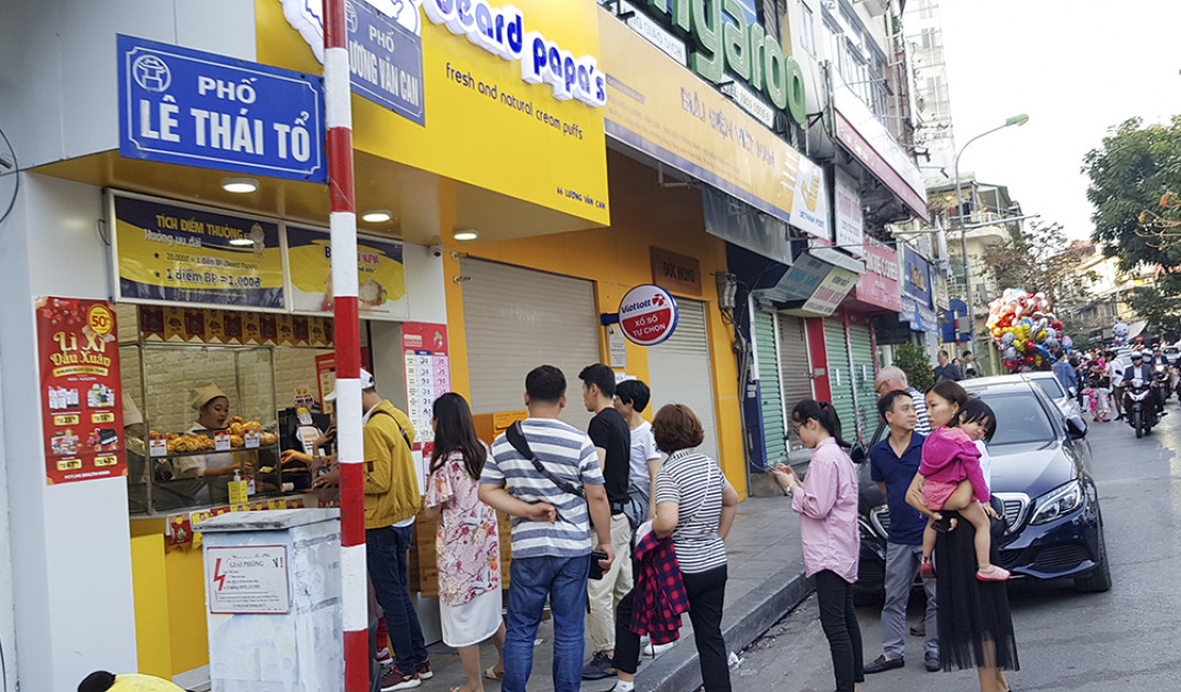 Một cửa hàng bánh với hàng dài người xếp hàng ra tận lòng đường để đợi mua.