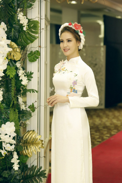 Áo được làm từ chất liệu gấm tơ tằm hoa chìm màu trắng, đặc biệt phù hợp cho các cô dâu yêu thích sự nhẹ nhàng, thanh lịch. Trên thân áo là những bông hoa đa sắc, được phối hợp cầu kỳ cả về kỹ thuật màu sắc. Áo từng được Hoa hậu Việt Nam 2014 Kỳ Duyên lựa chọn.