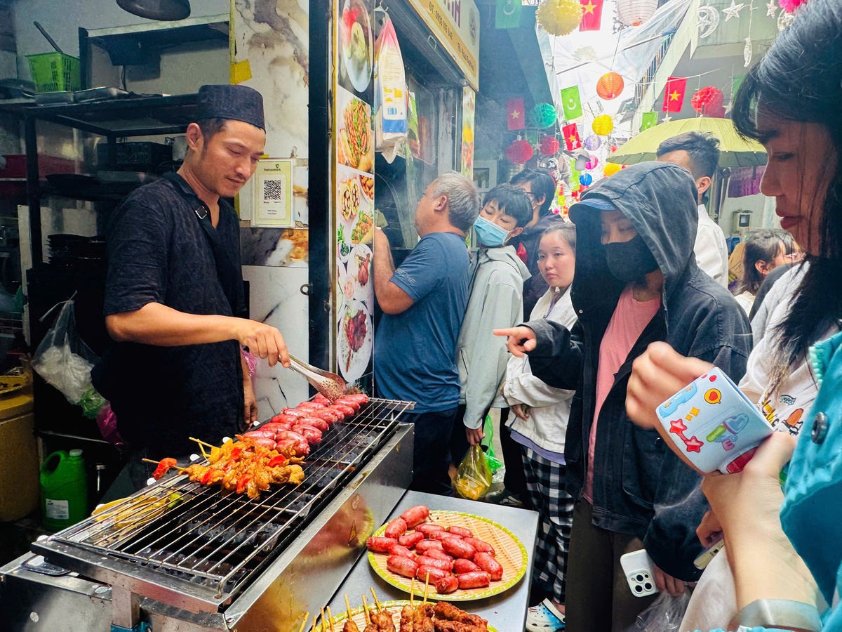 Rất đông người dân chờ mua Tung lò mò - lạp xưởng bò truyền thống của người Chăm - được nướng giòn ruộm. Lớp mỡ bò chảy nhẹ, dậy mùi thảo mộc. Món này thường ăn kèm đồ chua, vị béo xen lẫn chua ngọt, dễ gây "nghiện" với thực khách lần đầu thử. Ảnh: Hồ Lam