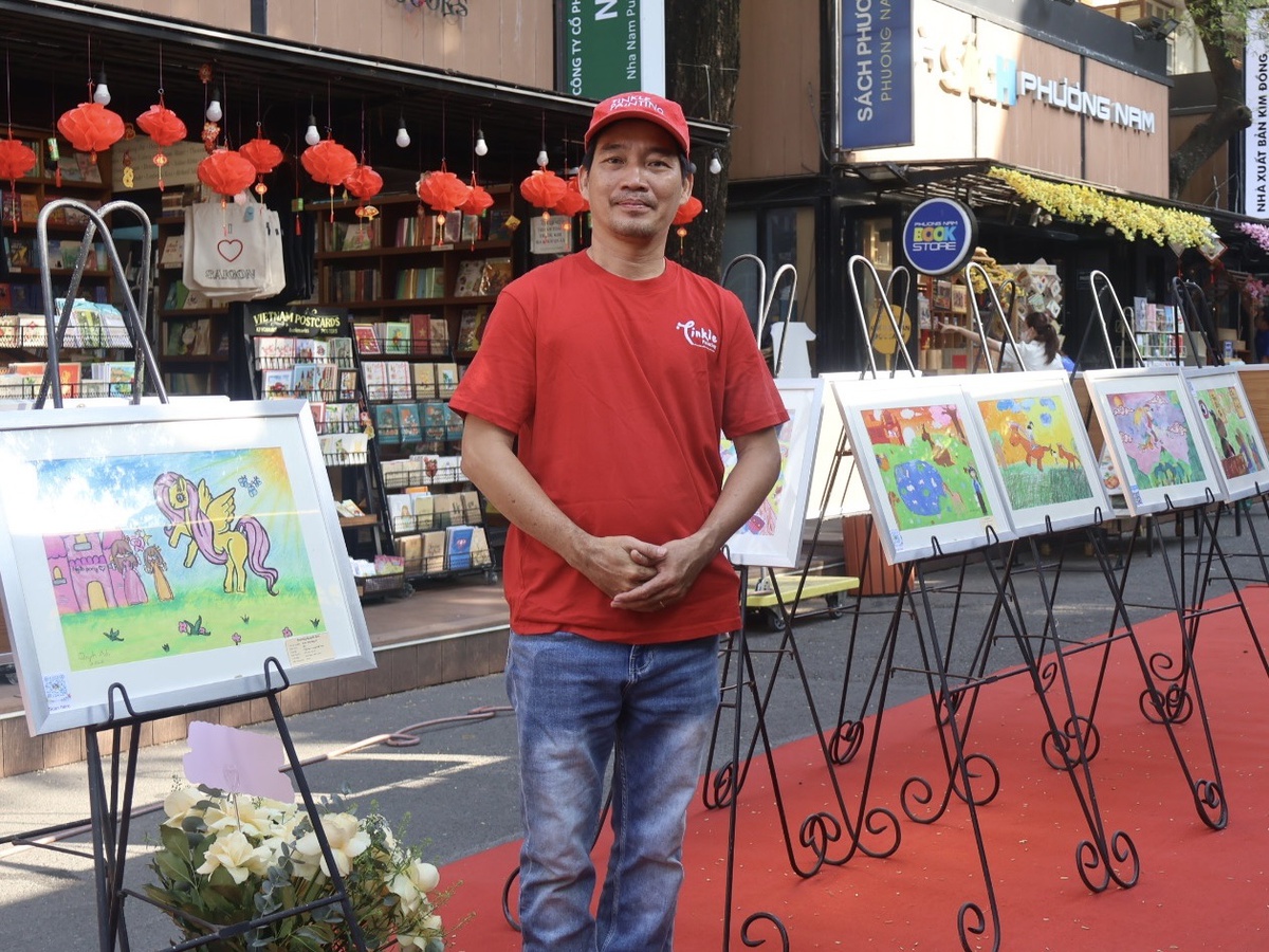 Hoạ sĩ Thành Nhân đứng cạnh các tác phẩm trưng bày của học trò mình. Ảnh: Hồ Lam