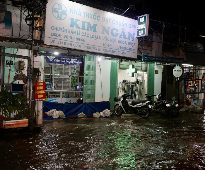 Một số cửa hàng bán nhu yếu phẩm như tiệm thuốc, cửa hàng tạp hoá vẫn sáng đèn buôn bán, đồng thời nỗ lực lấy tấm bạt, bao cát chắn để tránh nước vào. Ảnh: Hồ Lam Một số cửa hàng bán nhu yếu phẩm như tiệm thuốc, cửa hàng tạp hoá vẫn sáng đèn buôn bán, đồng thời nỗ lực lấy tấm bạt, bao cát chắn để tránh nước vào. Ảnh: Hồ Lam