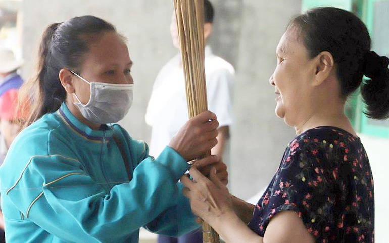 Chị Bùi Thị Lợi (trái) hỗ trợ, hướng dẫn một người khiếm thị lớn tuổi bó chổi