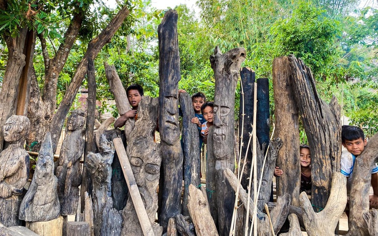 Trẻ em làng Kon K’tu bên những bức tượng gỗ do người làng tạc.